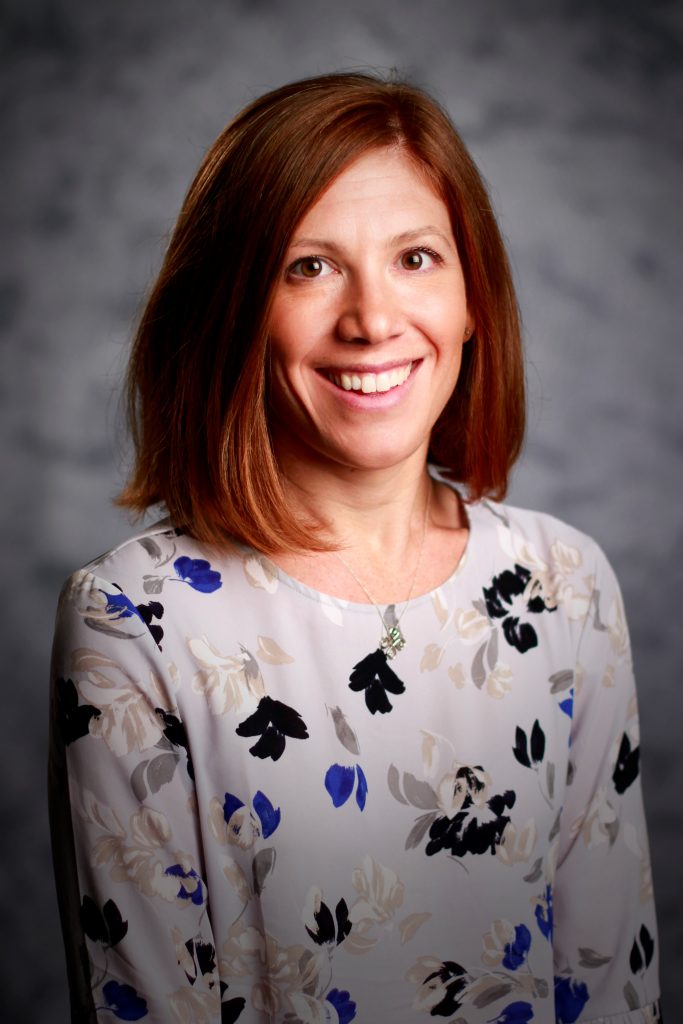 Headshot of seminar speaker, Dr. AnnMarie Walton, wearing a gray floral long-sleeve top, against a gray background