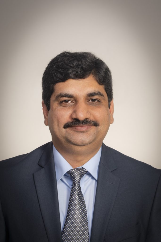 Formal headshot of seminar speaker, Dr. Salik Hussain, wearing a gray-blue suit and tie