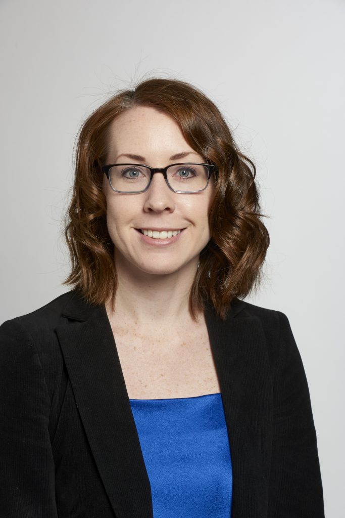 Formal headshot of seminar speaker, Dr. Alison Sanders, wearing a black suit jacket over a navy blue top