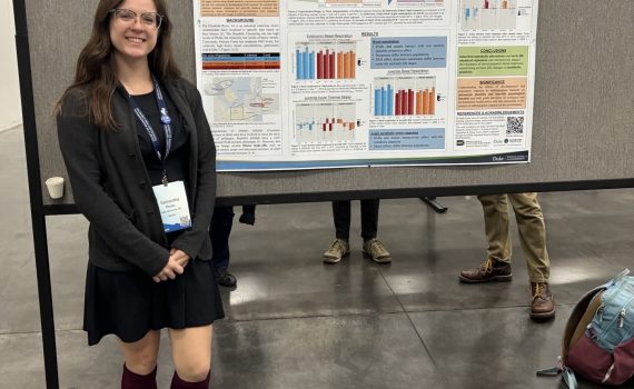 3rd-year ITEHP student, Samantha Phelps, smiling, standing in front of her poster.