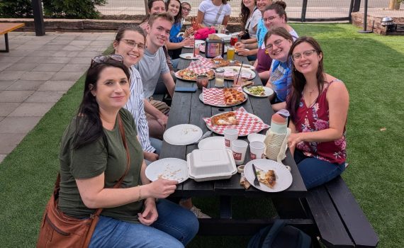 May ITEHP Toast attendees, sitting at a picnic table, with pizza and salad for dinner.