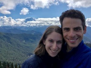 A couple smiles on top of a mountain